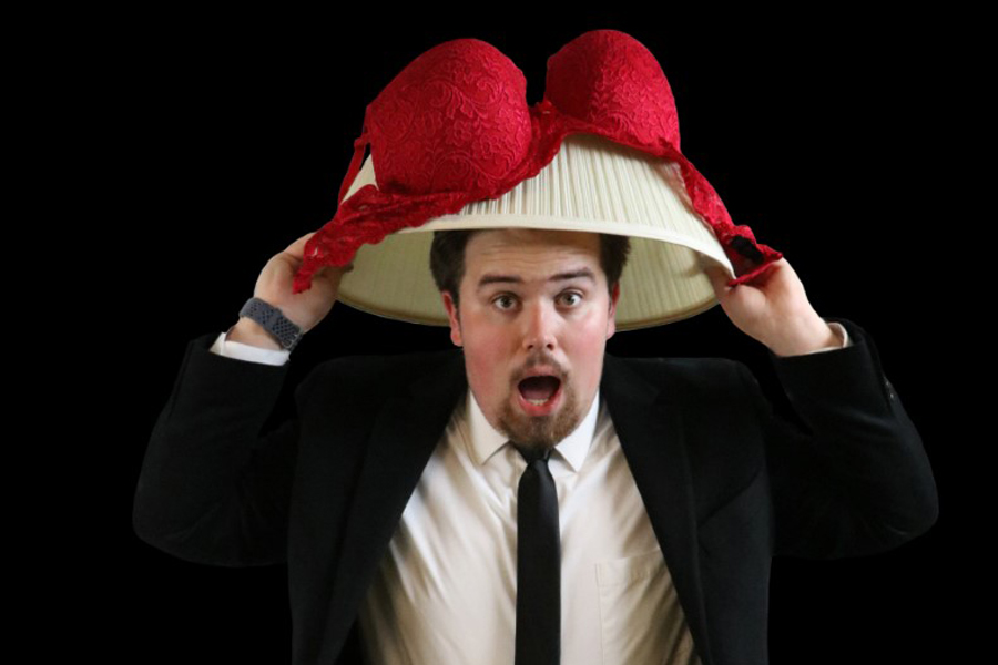 Man wearing a lampshade and a red bra on his head.